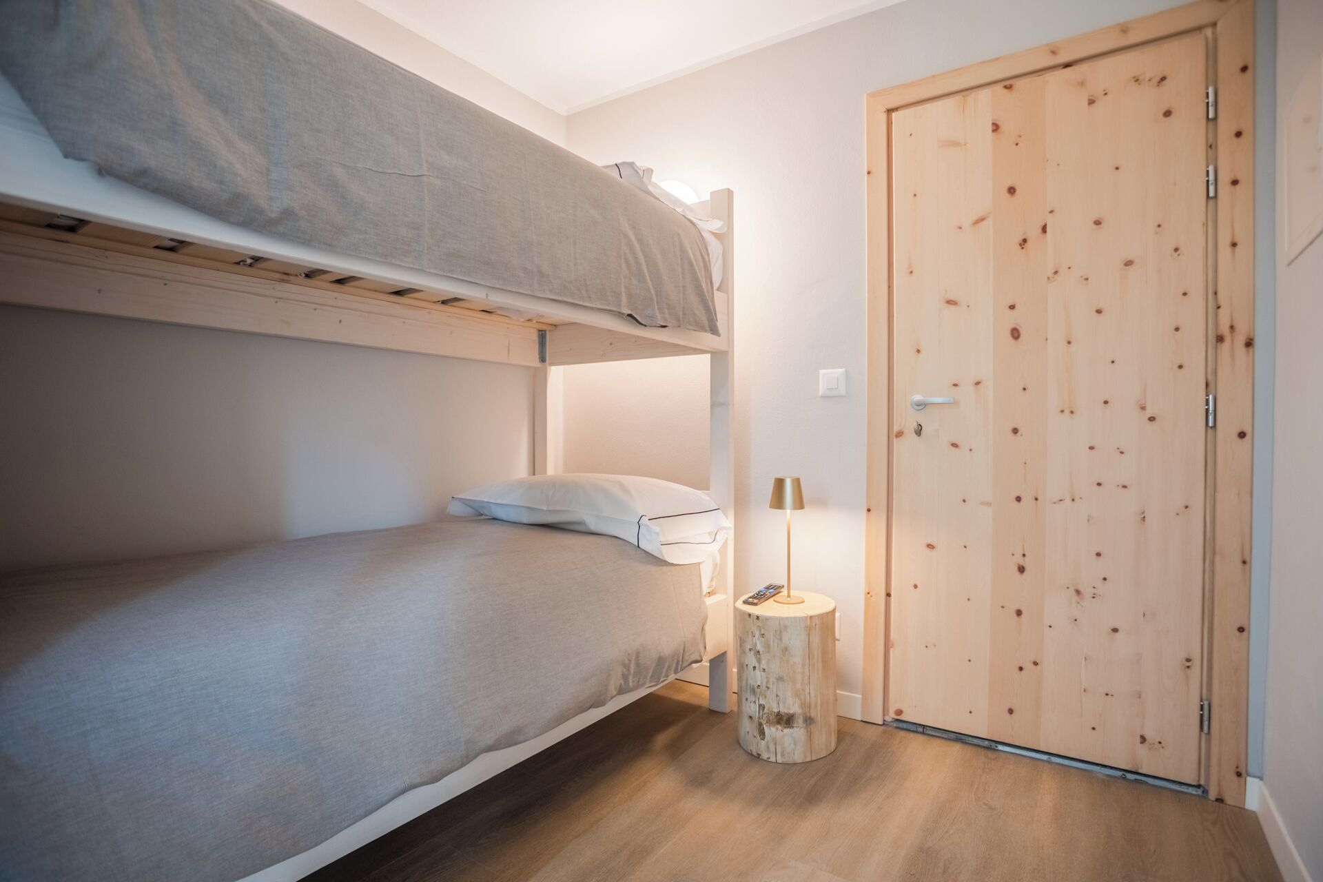 A bunk bed room with a wooden door and a small round wooden stool.