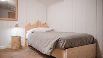 Un dormitorio con una cama de madera, una mesita de noche redonda con una lámpara y un espejo grande en la pared.