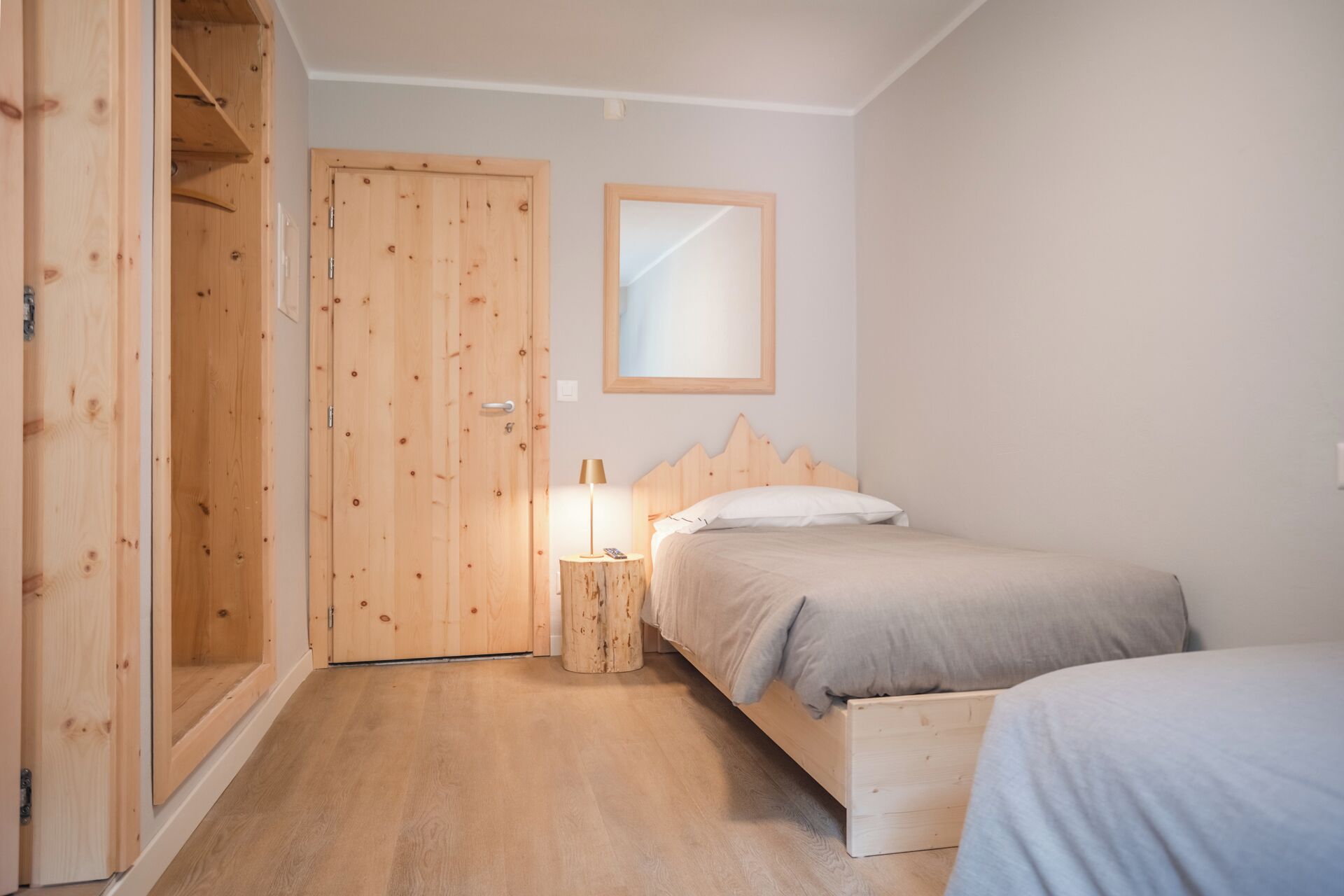 A bedroom with a wooden wardrobe, a bed with a wooden headboard, and a bedside table with a lamp.