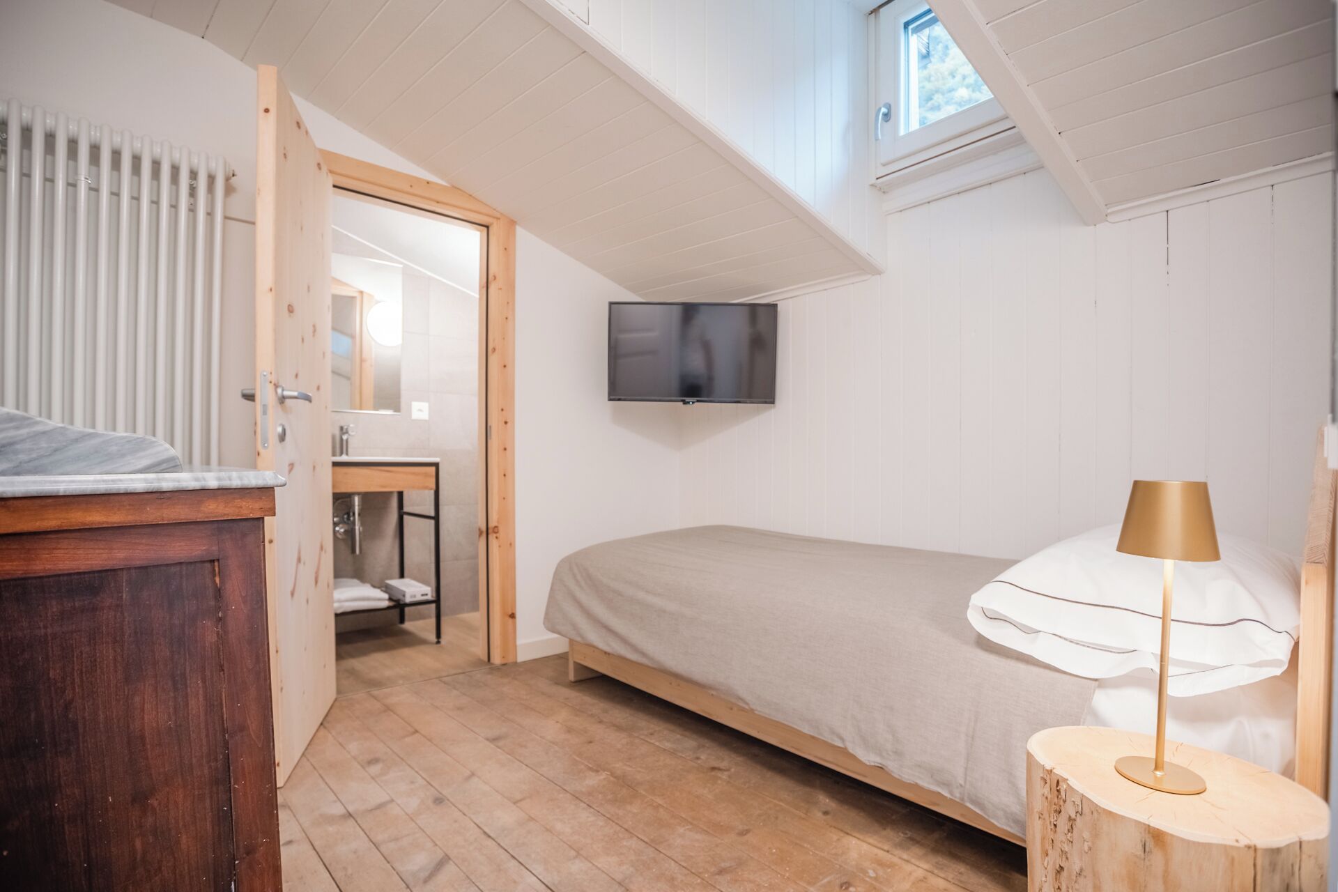 A bedroom with a wooden bed, a bedside lamp, a TV mounted on the wall, and a wooden floor.