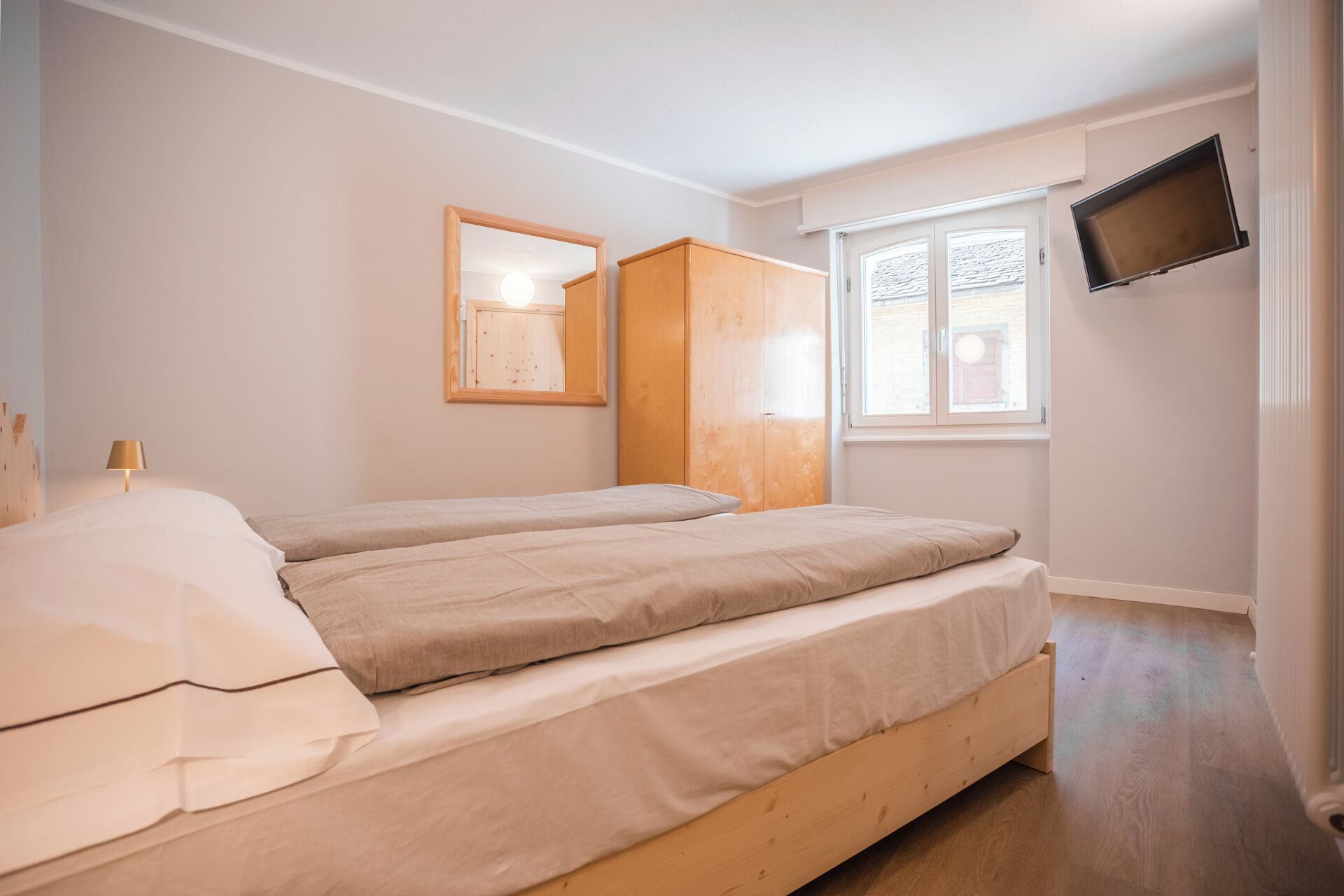 Habitació amb dos llits, un armari de fusta, un mirall, una televisió i una finestra.
