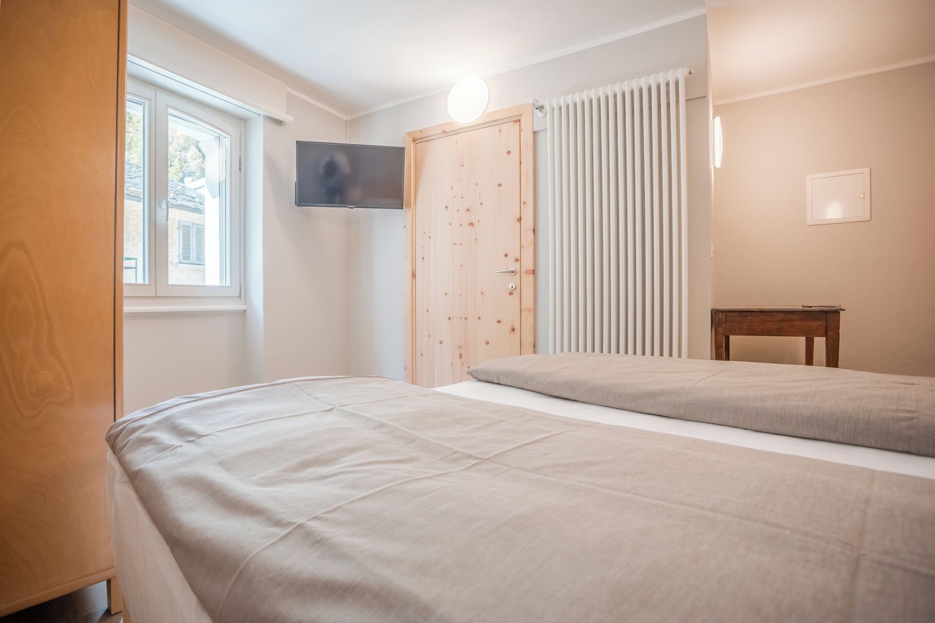 A bedroom with two beds, a TV mounted on the wall, a wooden wardrobe, and a radiator.
