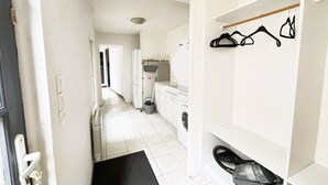 A hallway leading to a laundry area with a washing machine, dryer, and a shoe rack with hangers. - Gîte des Débats, ideal for families and friends. Pets welcome! (Valence-en-Poitou)