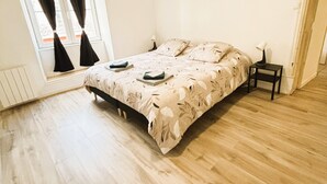 A bedroom with a bed, a nightstand, a window with curtains, and a radiator. - Gîte des Débats, ideal for families and friends. Pets welcome! (Valence-en-Poitou)