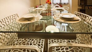 A dining area with a glass table surrounded by white chairs, a black pendant light, and a window with curtains. - Gîte des Débats, ideal for families and friends. Pets welcome! (Valence-en-Poitou)