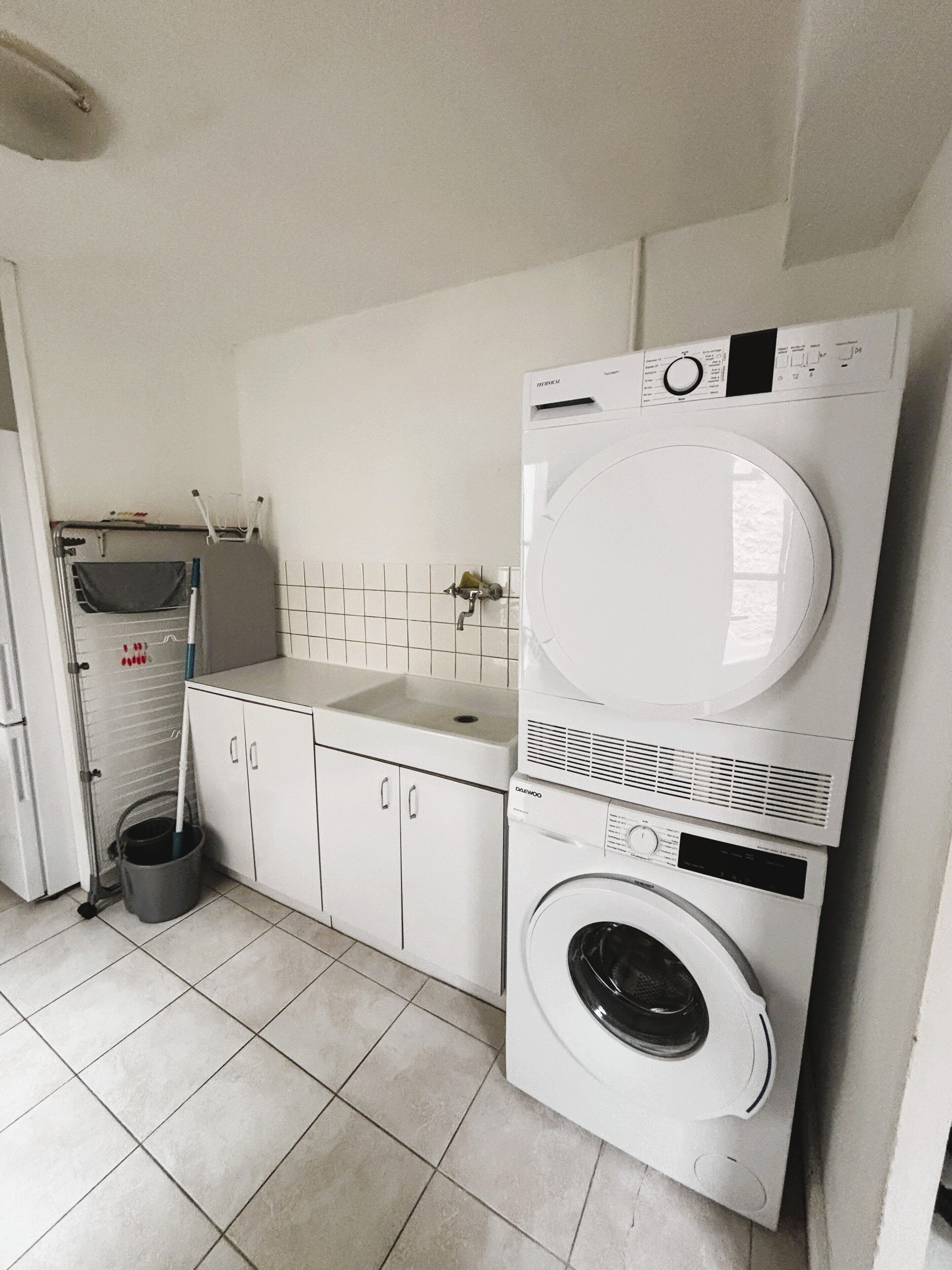 A laundry room with a stacked washer and dryer, a sink, and a mop bucket.