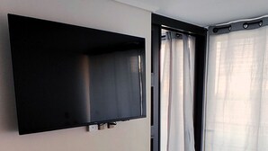 A bedroom with a bed, a flat-screen TV mounted on the wall, a window with curtains, and a tiled floor. - Movistar Arena | National Stadium | Caupolicán (Santiago)