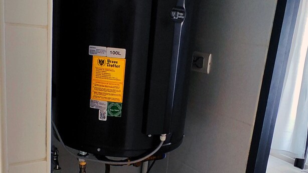 A compact room with a black heater, a Samsung washing machine, and a bed with a gray cover. - Movistar Arena | National Stadium | Caupolicán (Santiago)
