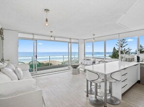 A modern kitchen with a large island, bar stools, and a view of the ocean. - Oceanfront Serenity At Main Beach (Main Beach)