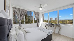 Quarto moderno com uma cama grande, ventilador de teto e vista para edifícios da cidade.