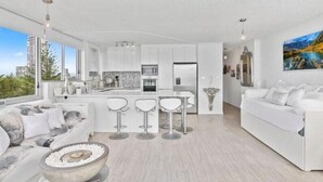 Uma sala de estar moderna com um sofá branco, uma mesa de centro e um espaço bar com banquetas.