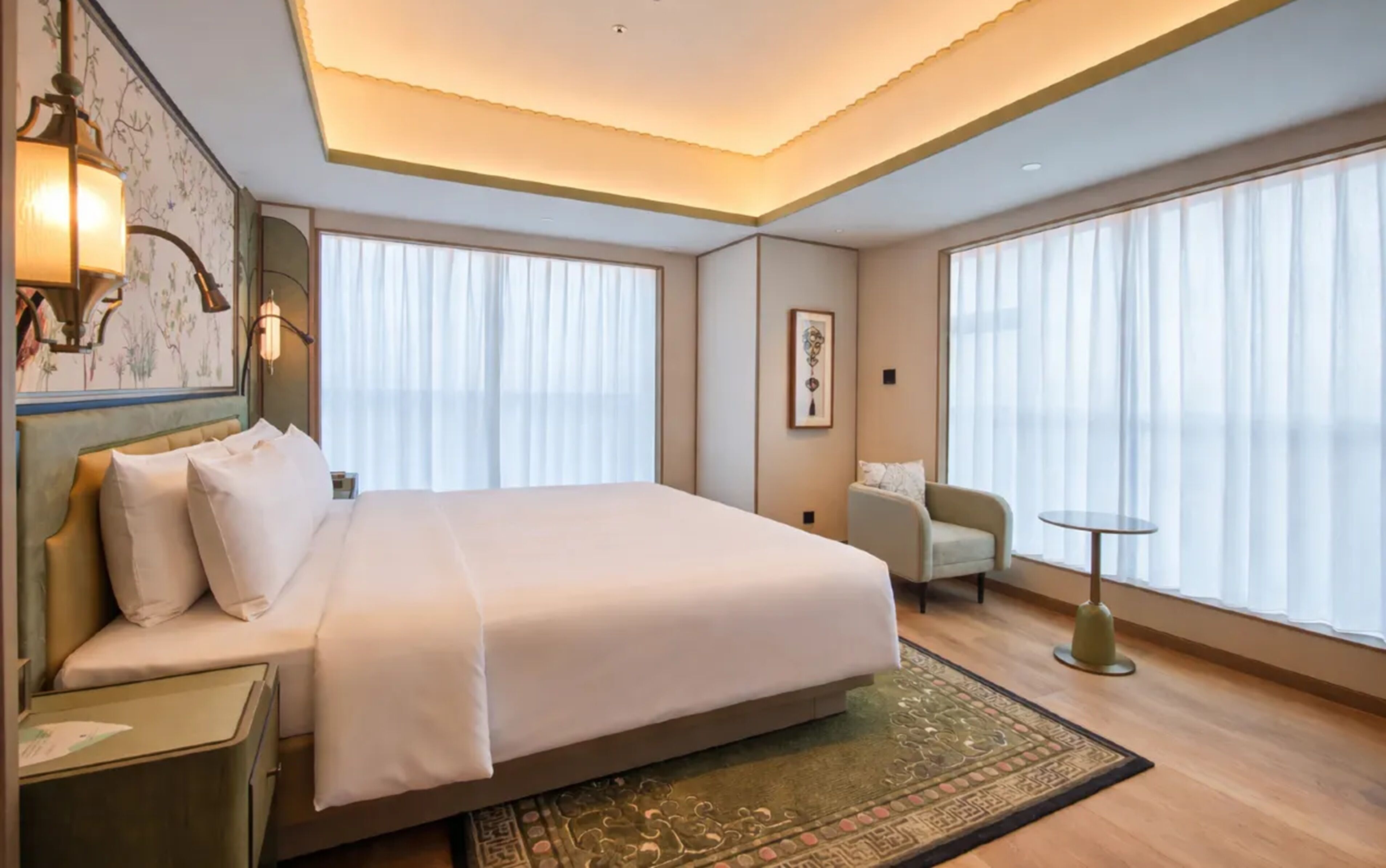 A hotel room with a large bed, a desk, a chair, and a small table.