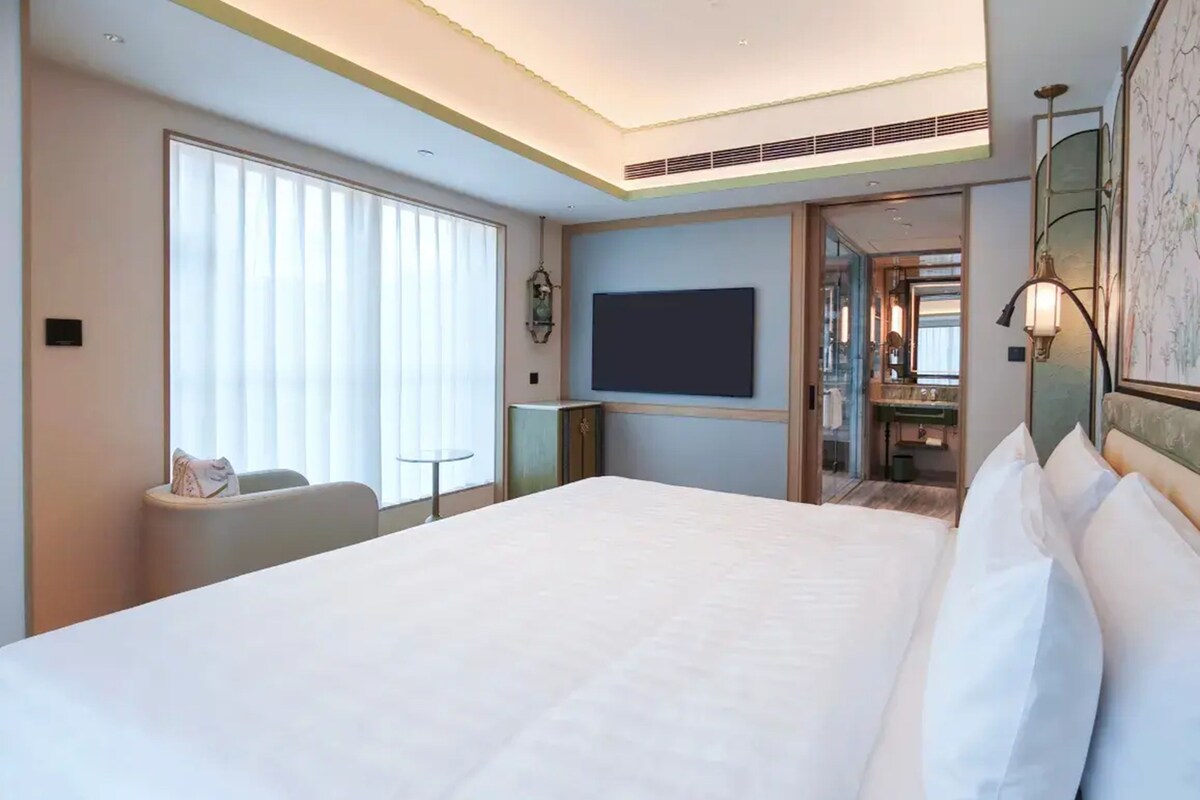 A hotel room with a large bed, a TV mounted on the wall, a small table, and a chair.