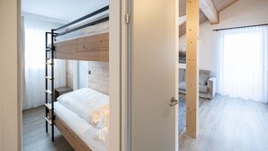 A bunk bed room with a wooden ladder, a door leading to a living area with a sofa and curtains.