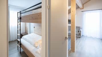 A bunk bed room with a wooden ladder, a door leading to a living area with a sofa and curtains.