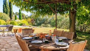 An outdoor dining area with a stone patio, wooden table, and chairs. - La Bergerie – Southern charm all year round (Tourrettes-sur-Loup)