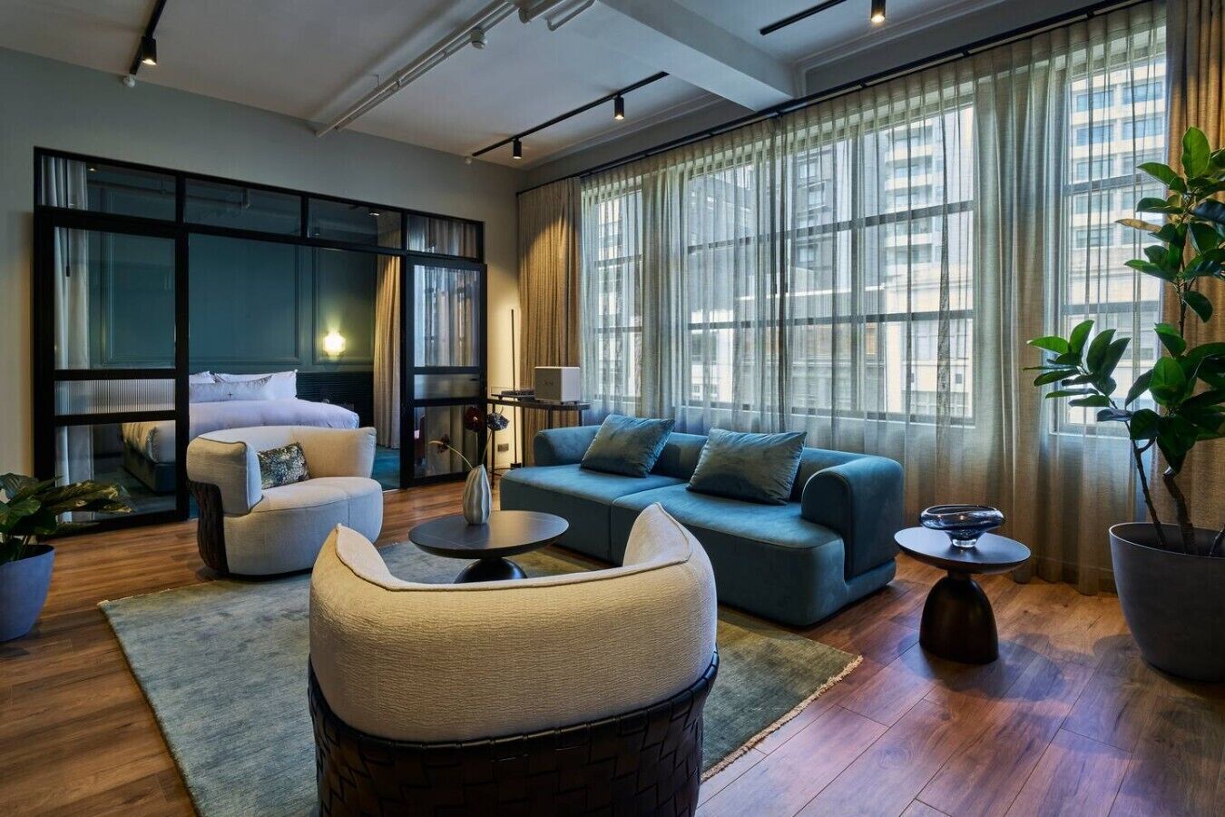 A modern living room with a sofa, armchair, and coffee table, large windows with curtains, and a potted plant.