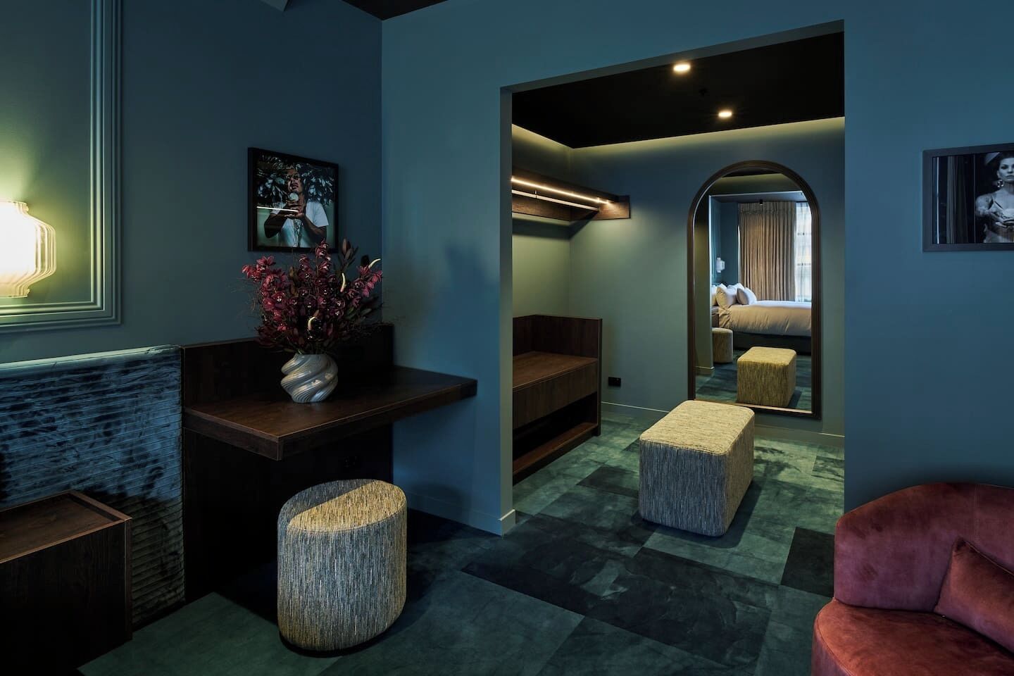 A modern interior with a seating area, a mirror, and a view into a bedroom.