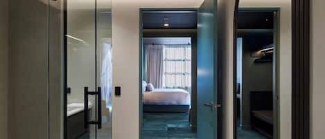 Una habitación de hotel moderna con un separador de vidrio, un espejo grande, una cama y un vestidor.