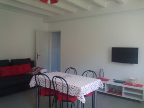 Un comedor con mesa y sillas, un sofá, un televisor y una puerta que da a otra habitación.