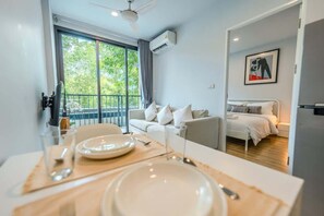 A modern hotel room with a balcony, a dining area with a table set for two, and a bed with a white headboard. - ZcapeX2 | Pool View & Fast Wifi (Choeng Thale, Thalang)