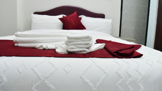 A neatly made bed with white linens and a red throw blanket, a red pillow, and a folded white towel on the bed. - Araka Homes-Naka/Exquisite 2 Bedroom Apartment (Nakuru)