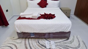 A neatly made bed with white linens and a red accent pillow, a small bedside table with a lamp, and a wooden wardrobe. - Araka Homes-Naka/Exquisite 2 Bedroom Apartment (Nakuru)