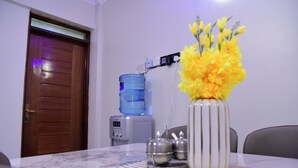 A room with a wooden door, a water dispenser, a vase with yellow flowers, and a table with a marble top. - Araka Homes-Naka/Exquisite 2 Bedroom Apartment (Nakuru)