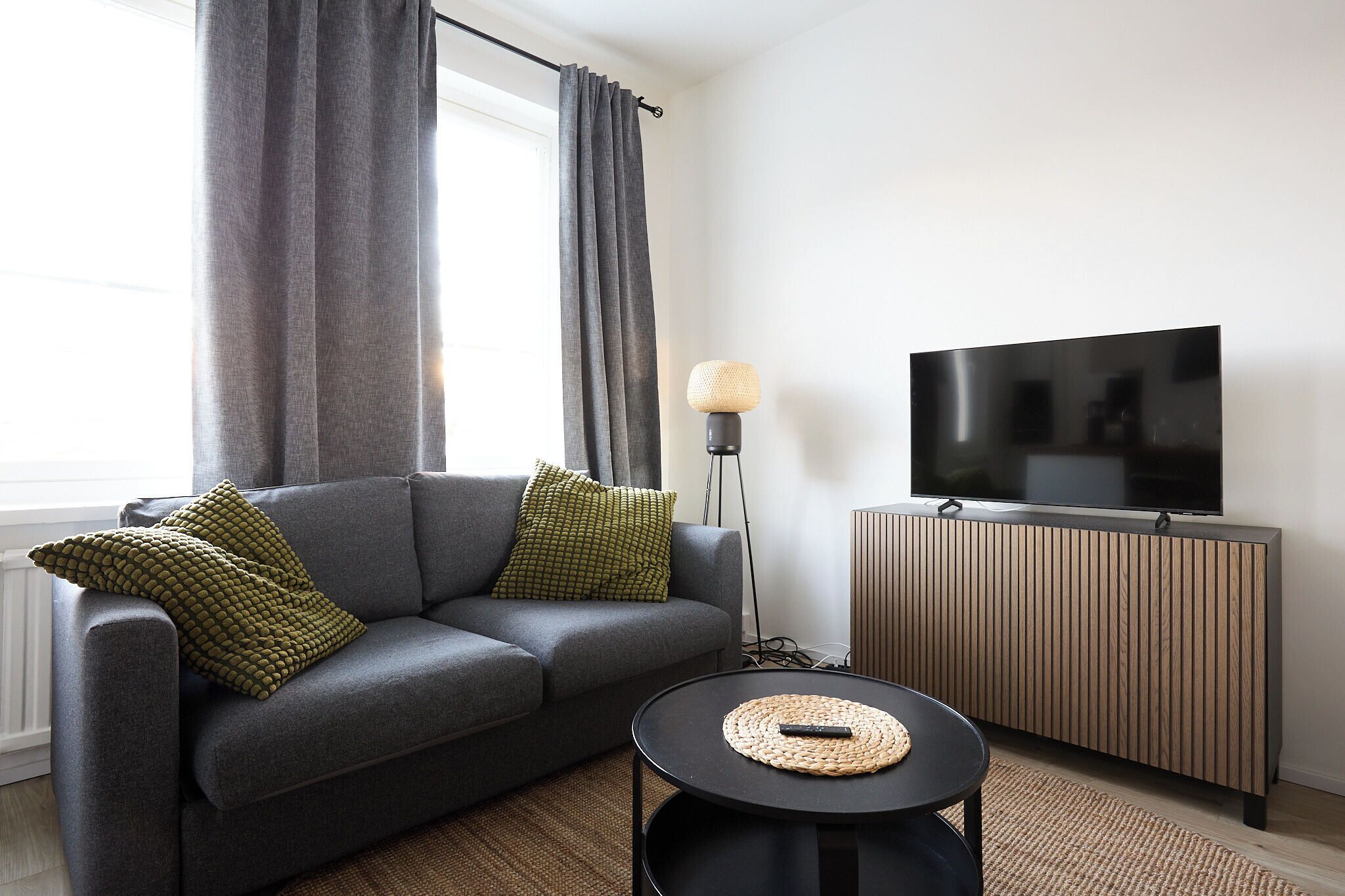 A modern living room with a grey sofa, a round coffee table, a TV on a wooden cabinet, and a floor lamp.