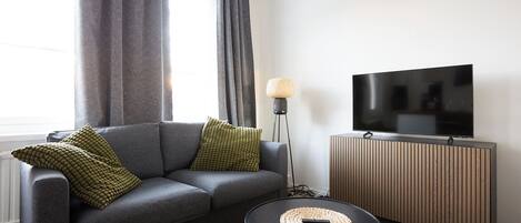 A modern living room with a grey sofa, a round coffee table, a TV on a wooden cabinet, and a floor lamp.