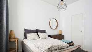 Une chambre à coucher bien rangée, avec un lit, une table de chevet, un miroir et une porte.