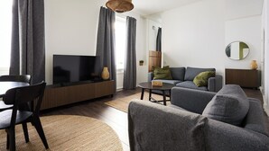 Un salon moderne doté d’un téléviseur à écran plat, de canapés gris, d’une table basse ronde et d’un luminaire suspendu en fibres tressées.