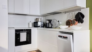 Une cuisine moderne avec des meubles blancs, un four encastré, une machine à café et un lave-vaisselle.
