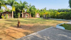 A spacious outdoor area with a volleyball net, surrounded by lush greenery and palm trees. - plumeria resort (Kushalnagar)