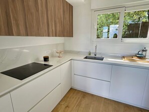 Una cocina moderna con armarios blancos, encimera negra y ventana con vista a la vegetación.