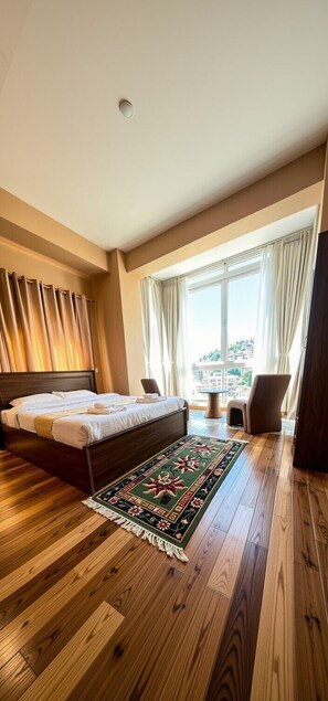 A hotel room with a large bed, a wooden floor, a view of the city, and a window with curtains. - GaiaYuel (Thimphu)