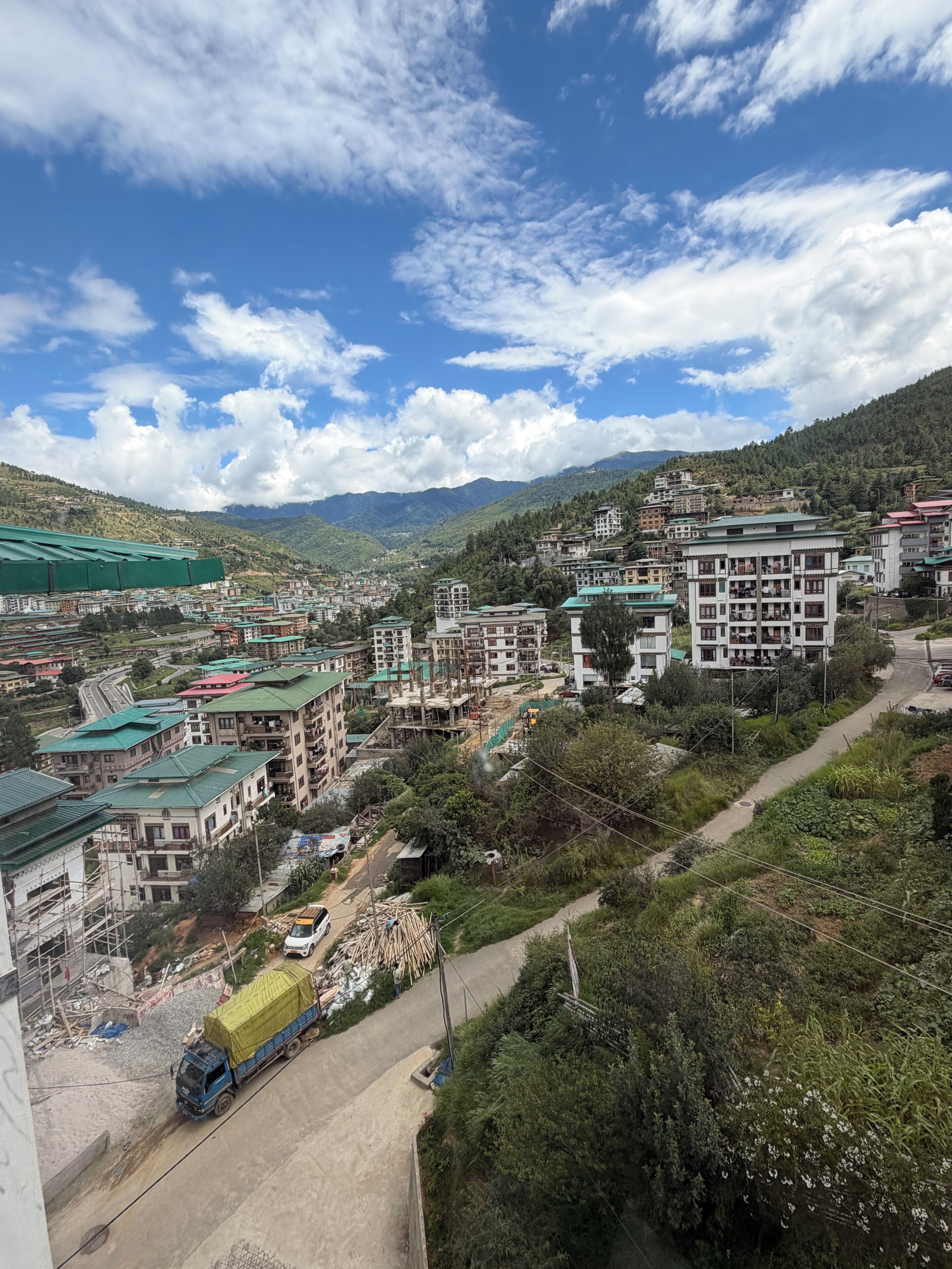A mountainous town with multi-story buildings, a winding road, and a truck parked on the side.