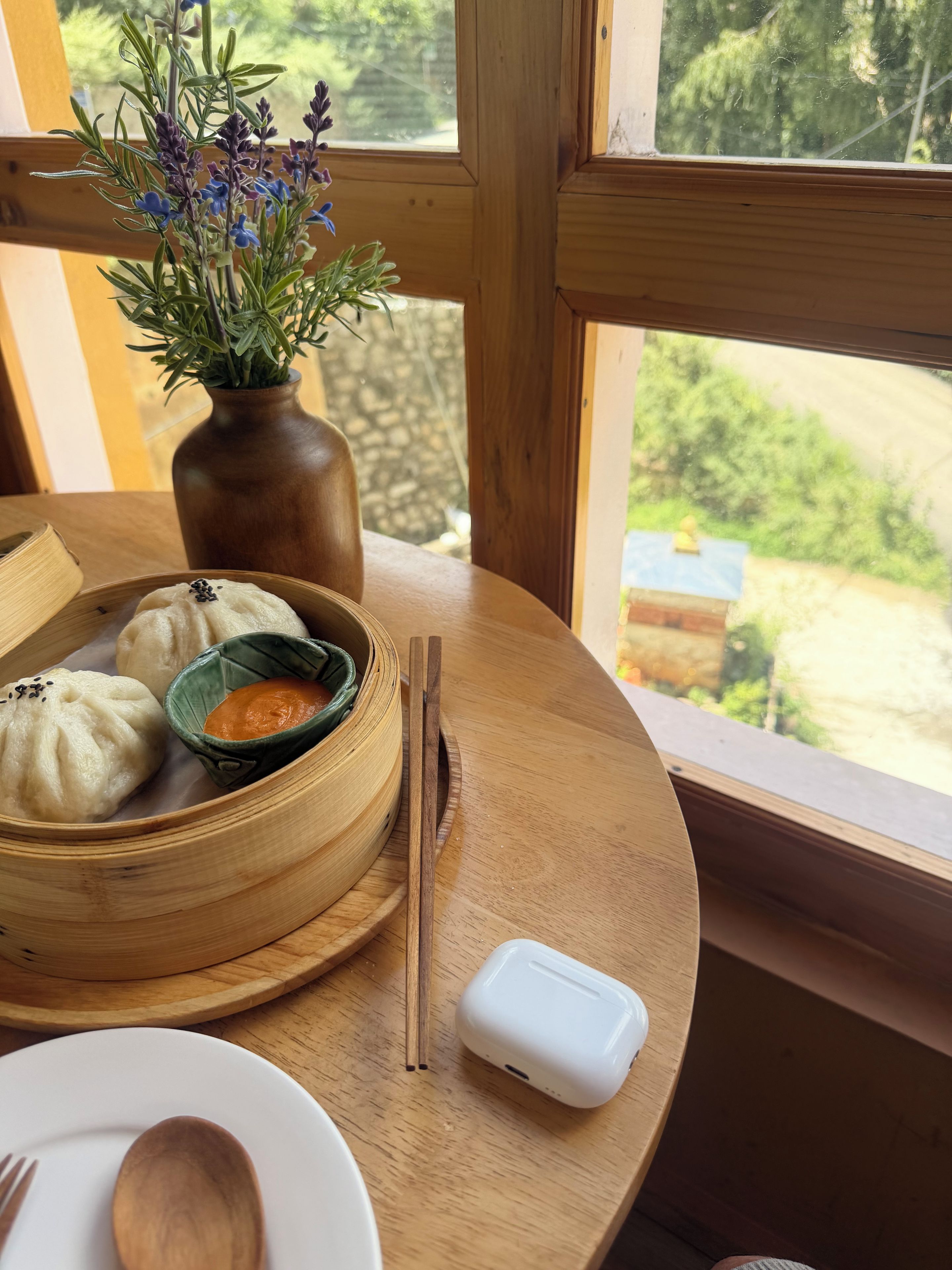 A table with a wooden table, a bowl of food, chopsticks, a spoon, and a white device.