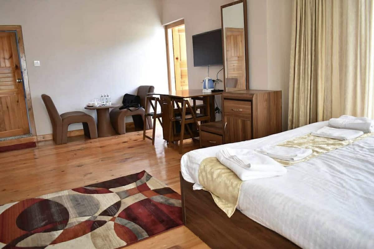 Una habitación de hotel con cama, escritorio, silla, televisor y piso de madera.