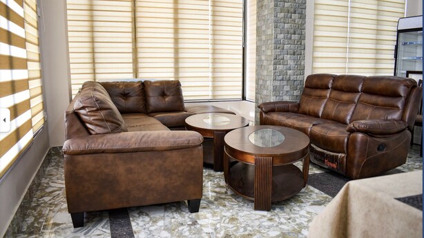 A living room with a sectional sofa, two round coffee tables, and a stone wall. - GaiaYuel (Thimphu)
