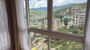 Quarto com uma janela grande com vista para uma paisagem montanhosa e edifícios.