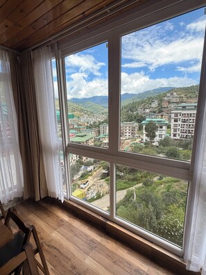 A room with a large window overlooking a mountainous landscape with buildings. - GaiaYuel (Thimphu)