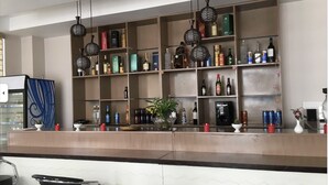 A bar area with shelves stocked with various bottles and cans, a decorative plant, and hanging light fixtures. - GaiaYuel (Thimphu)
