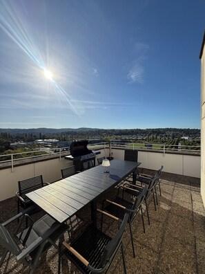 Eine Terrasse im Freien mit Tisch, Stühlen, einem Grill und Blick auf die Stadt.