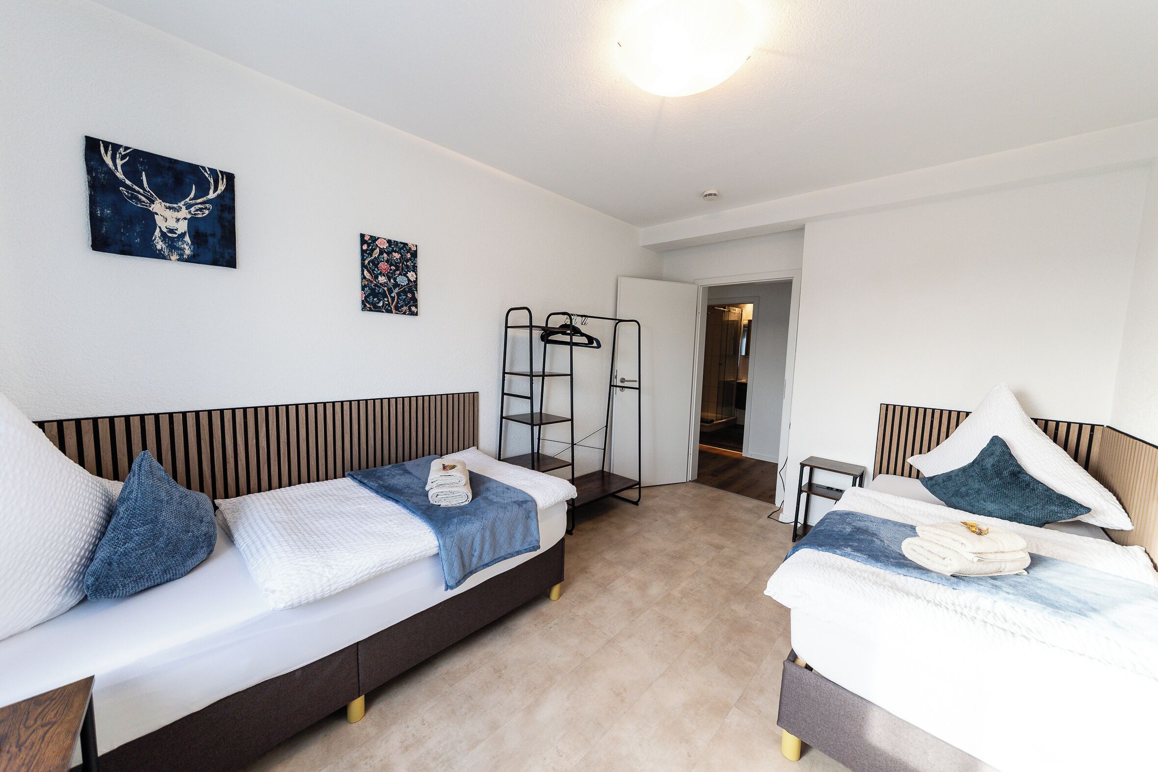Une chambre d’hôtel moderne équipée de deux lits simples, d’une armoire, d’un portant à vêtements et d’une porte donnant accès à la salle de bain.