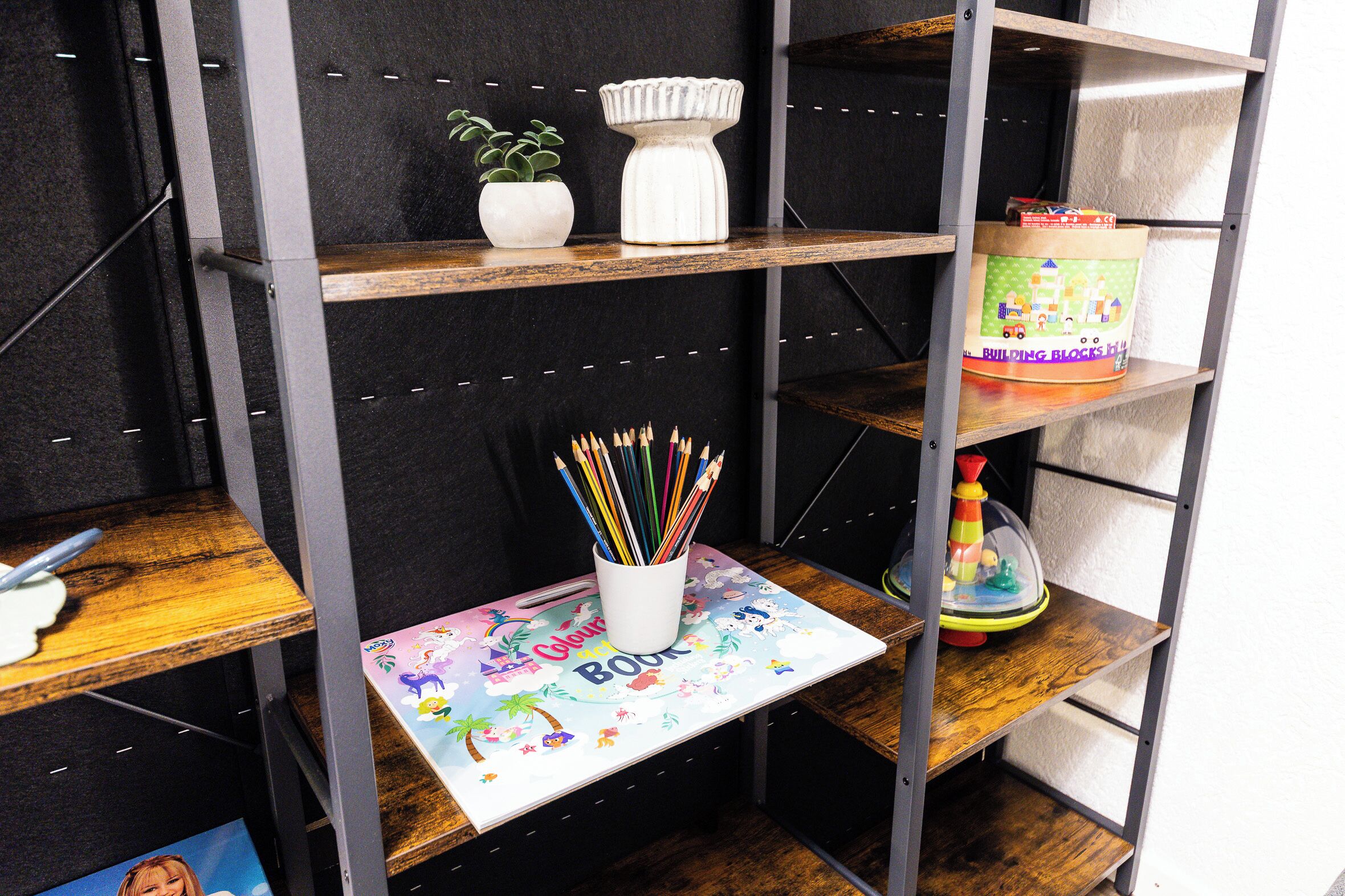 A shelf with a white vase, a small potted plant, and a colorful book titled "Coloring Book."