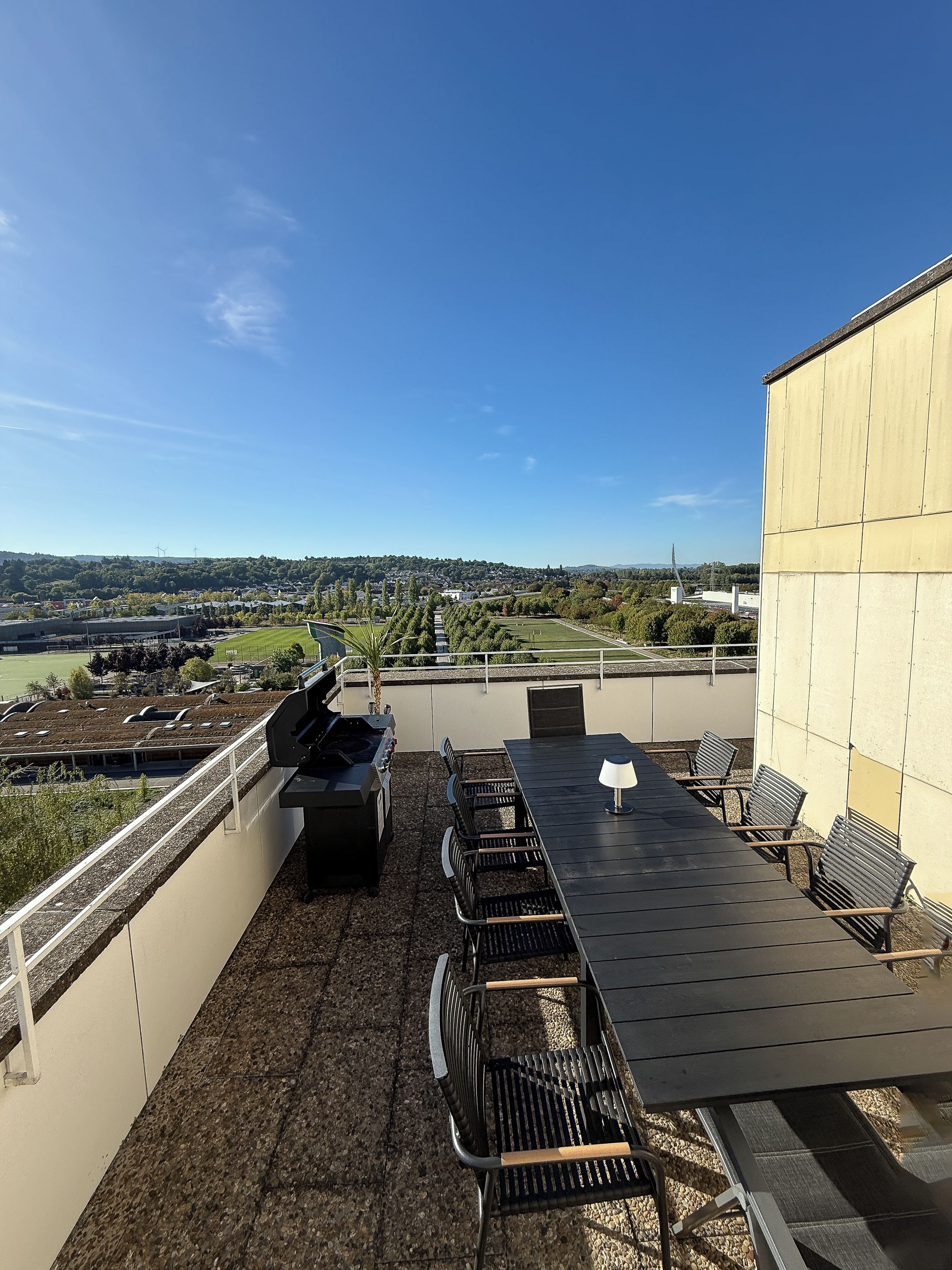 A rooftop terrace with a grill, seating, and a view of the cityscape.