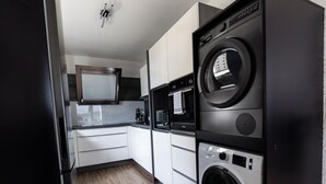 A compact kitchen with a black refrigerator, a microwave, a washing machine, and a built-in oven. - Holiday Apartment 120 m² Penthouse – Europa-Park – Strasbourg – Colmar (Lahr/Schwarzwald)