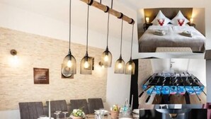 A modern dining area with a wooden table set for four, hanging pendant lights, and a view of a cozy bedroom with a bed and decorative pillows. - Holiday Apartment 120 m² Penthouse – Europa-Park – Strasbourg – Colmar (Lahr/Schwarzwald)