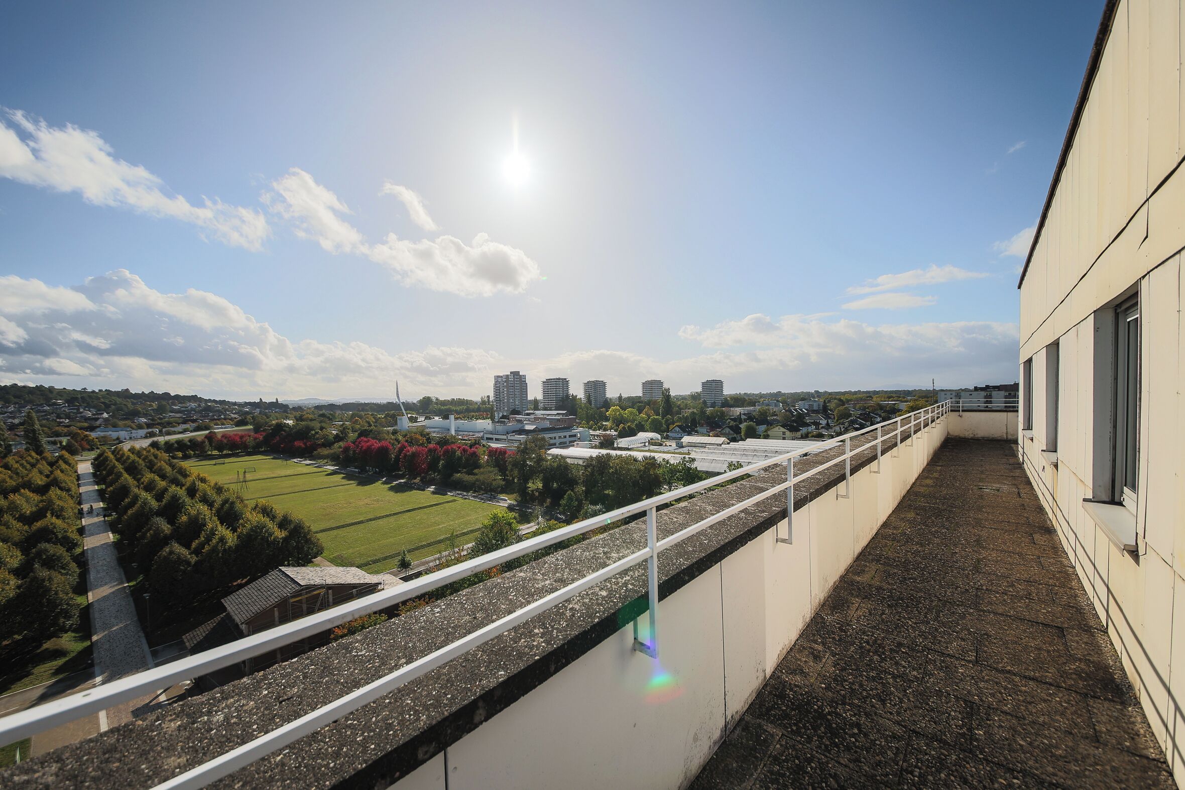 Ein Balkon mit Blick auf eine Stadtlandschaft, einschließlich Gebäude und einer grünen Wiese.